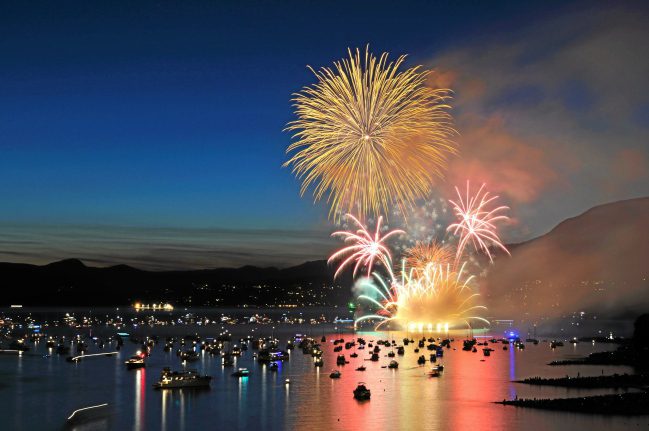 Fireworks over a body of water with boats in the background.