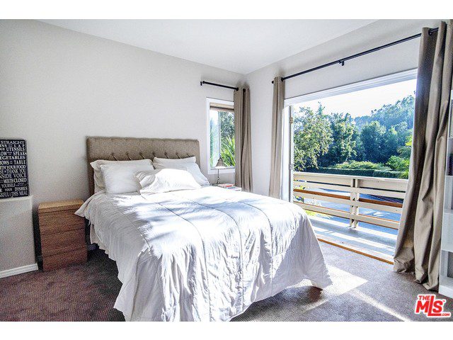 A bedroom with a balcony overlooking a wooded area.
