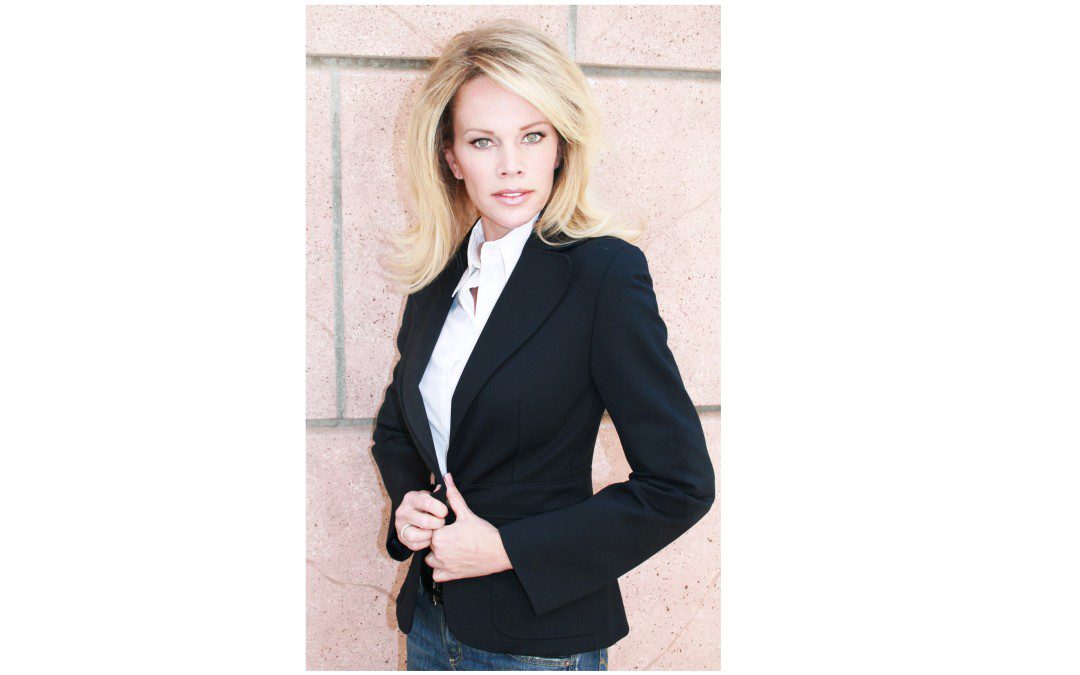 A woman in a black blazer leaning against a wall.