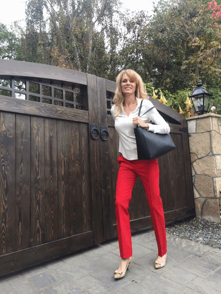 A woman in red pants standing next to a wooden gate.