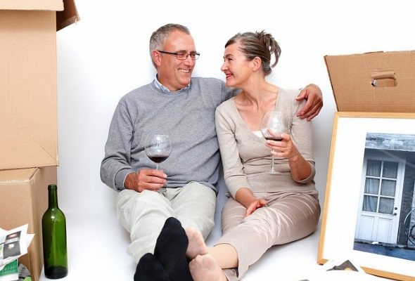 A couple sitting on the floor with boxes and a bottle of wine.